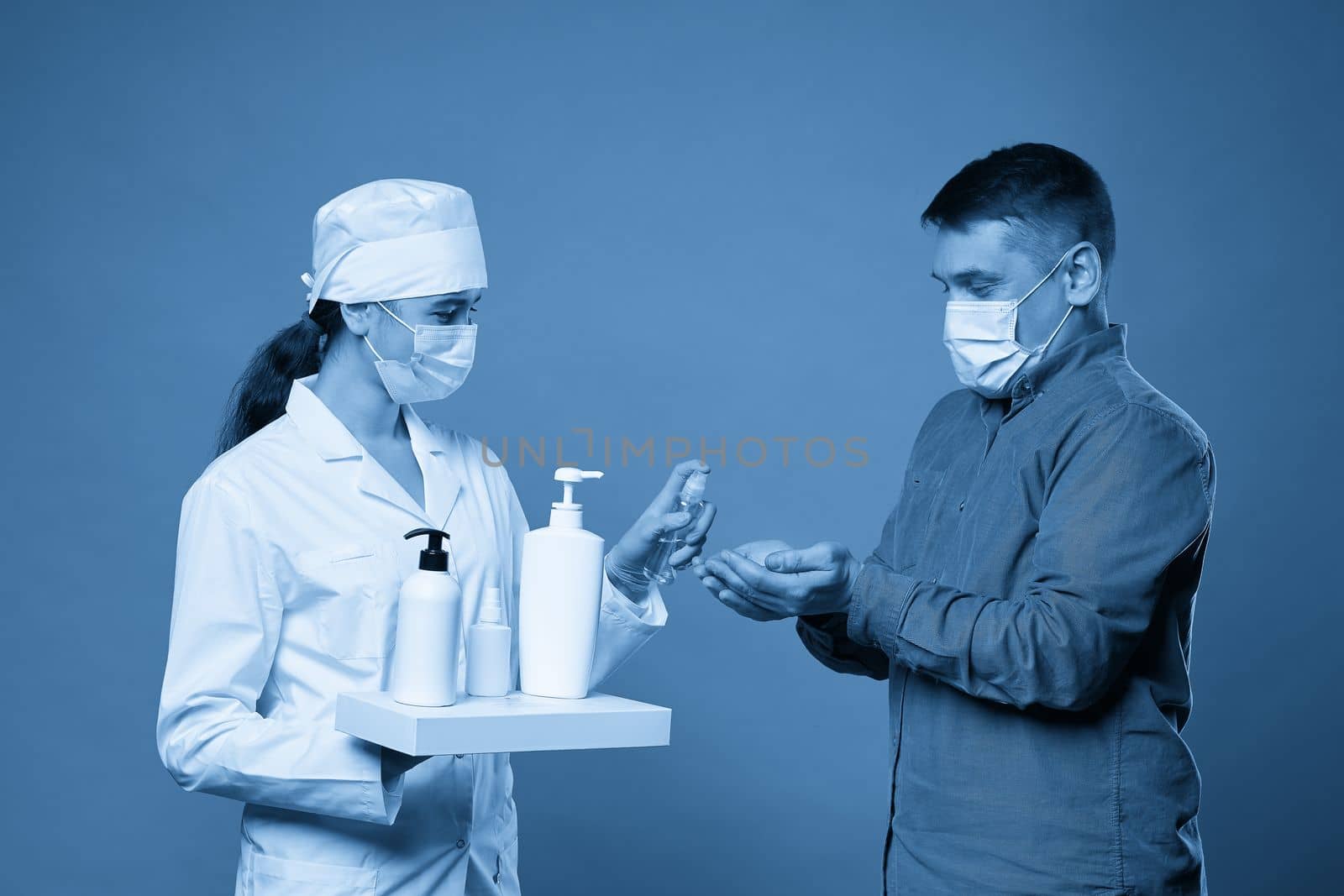 doctor applying antibacterial spray on patient hands on blue background by Mariakray