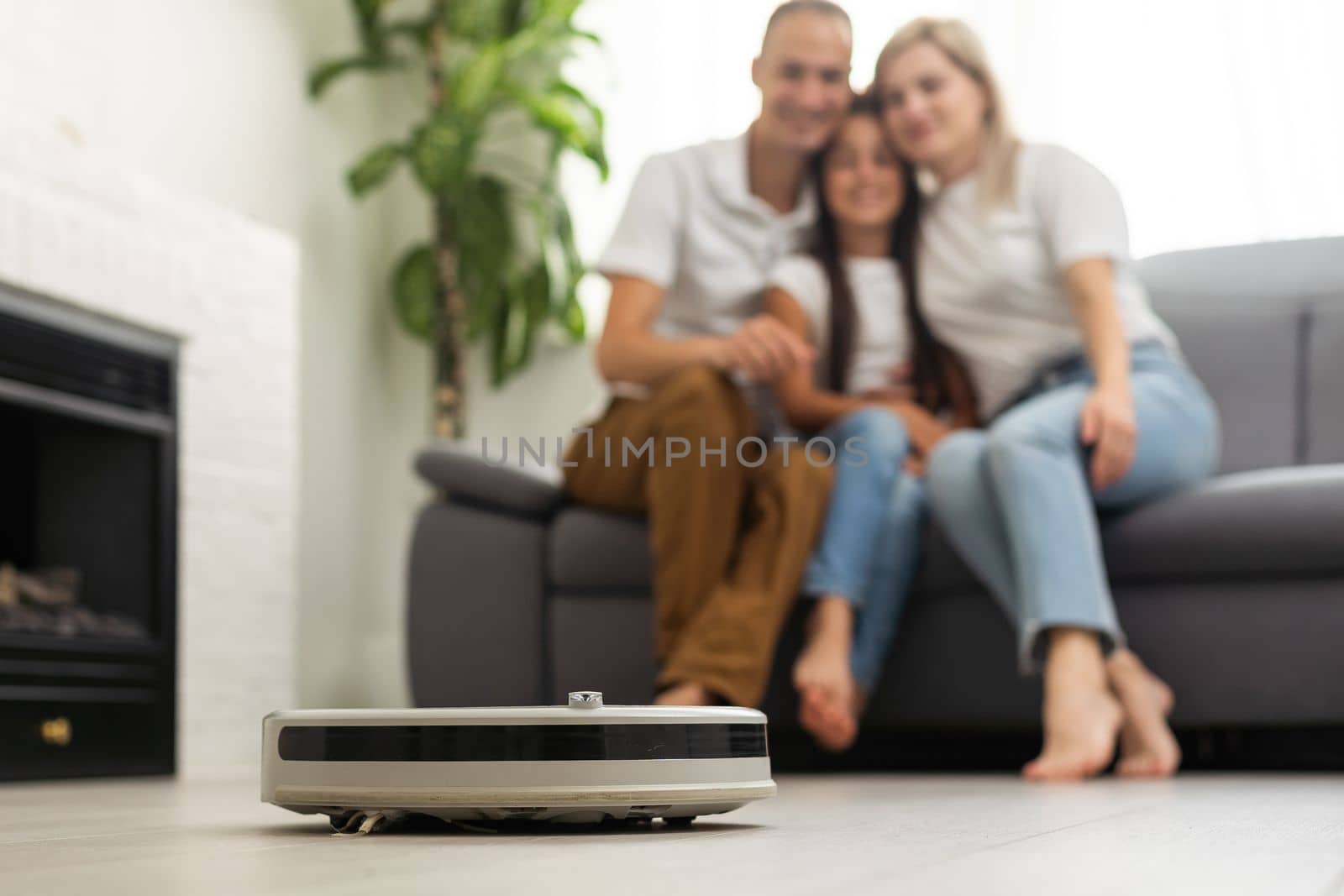 Young family resting on the couch while robotic vacuum cleaner doing its work at home. Household robots concept