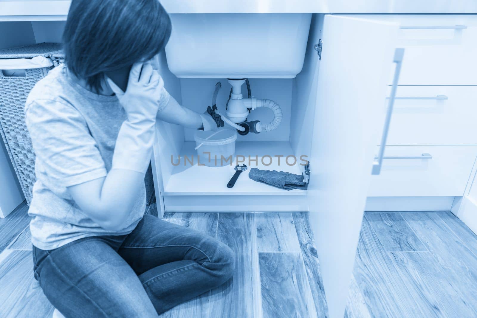 Woman sitting near leaking sink in laundry room calling for help by Mariakray