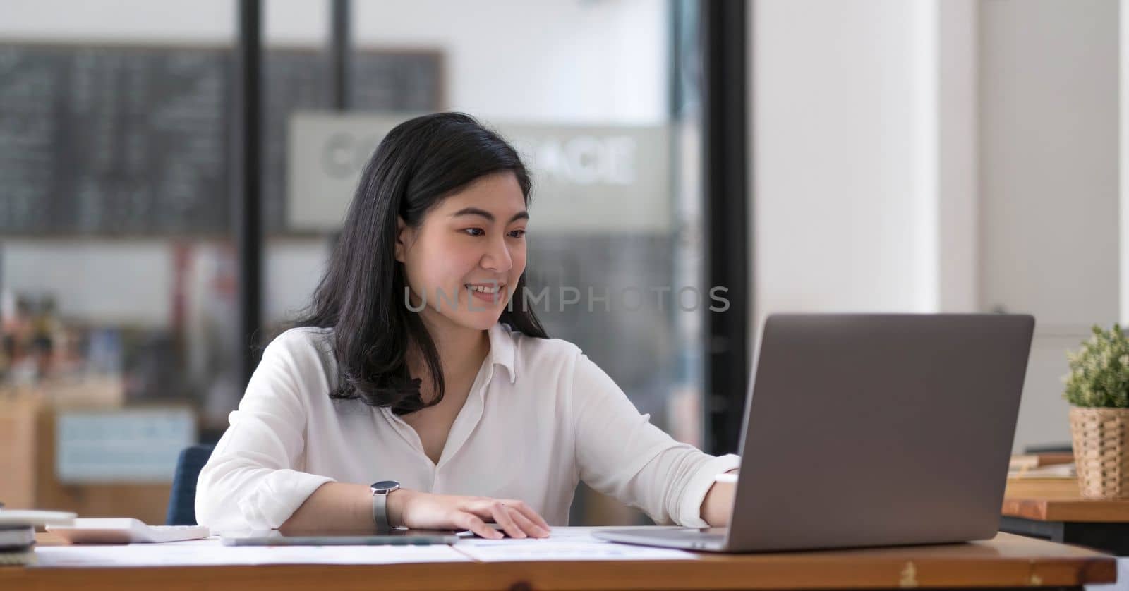Charming Asian businesswoman sitting in the office with a digital laptop computer. Excited Asian businesswoman raising hands to congratulate while working in a modern office,..