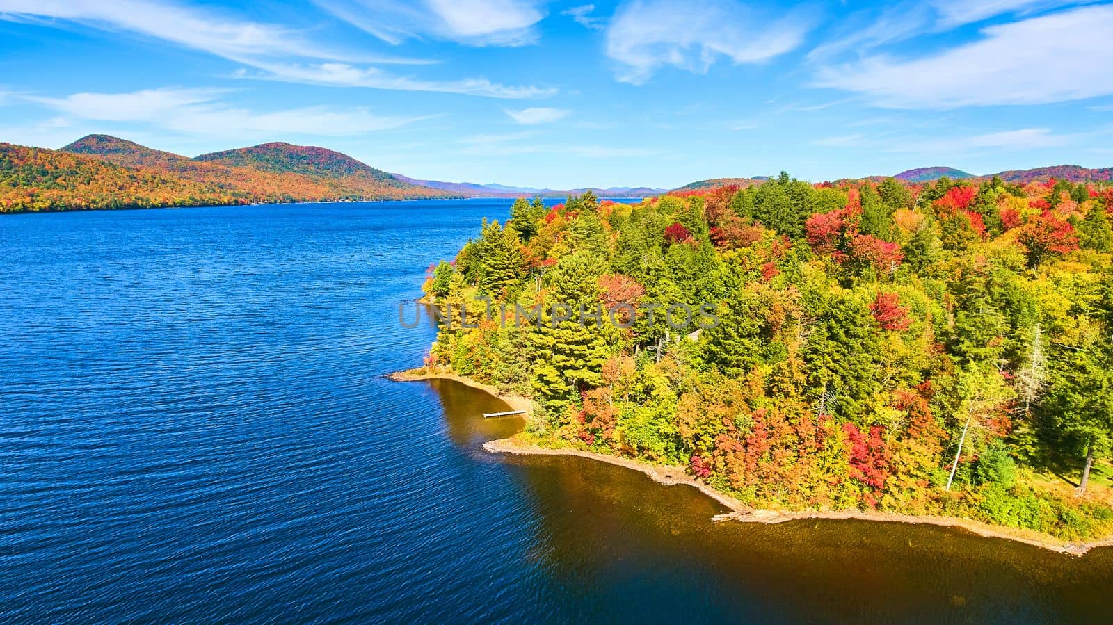 Aerial over lake with fall tree forest covering coast and blue waters by njproductions