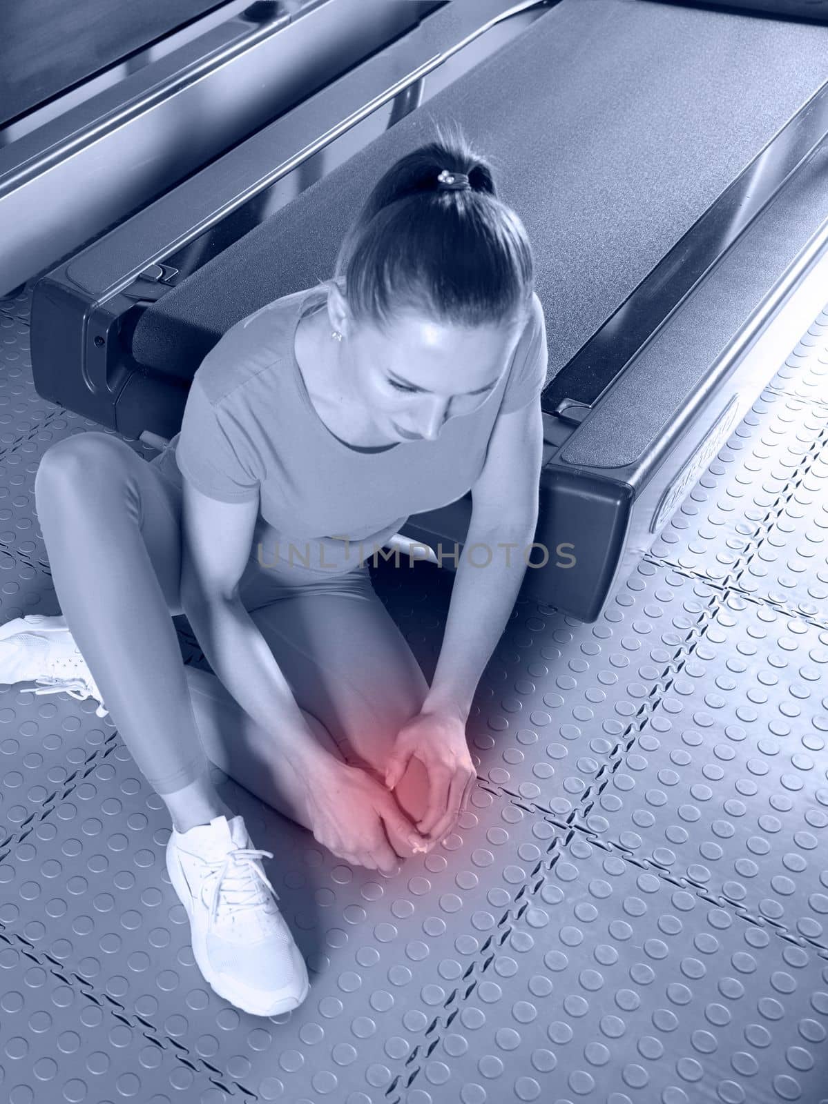 Young woman in sportswear having ache in knee while training in a gym, blue toning