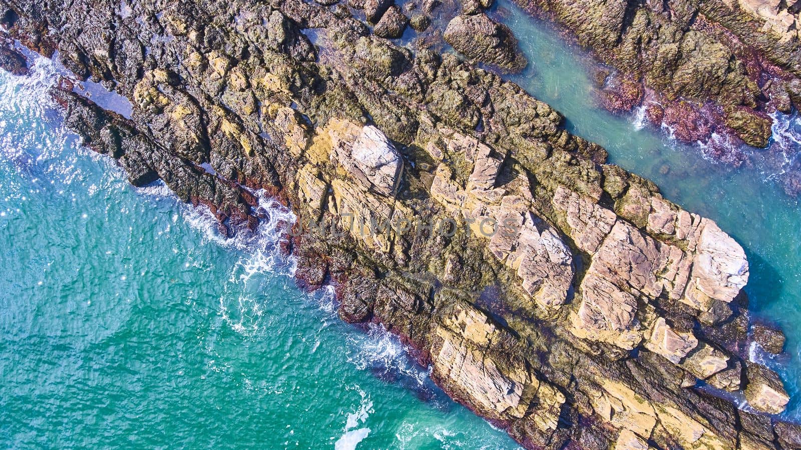 Aerial down of rocky coast section with crashing waves by njproductions