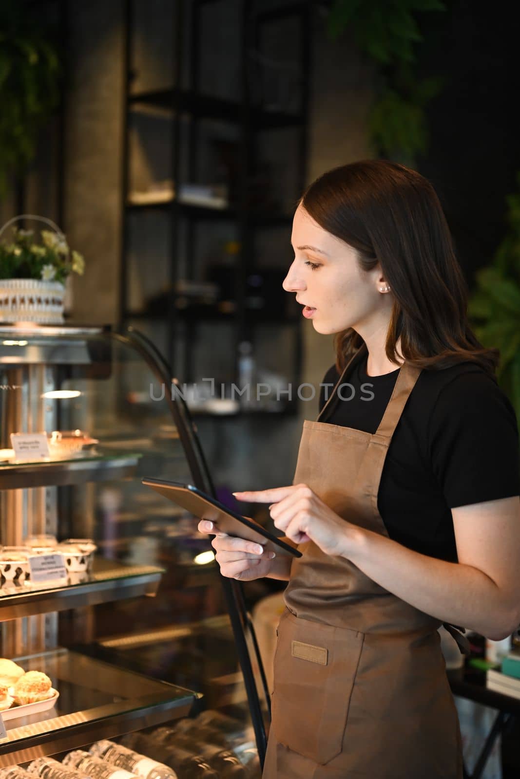 Beautiful caucasian woman coffee shop owner checking Inventory on digital tablet in a cozy loft style cafe.