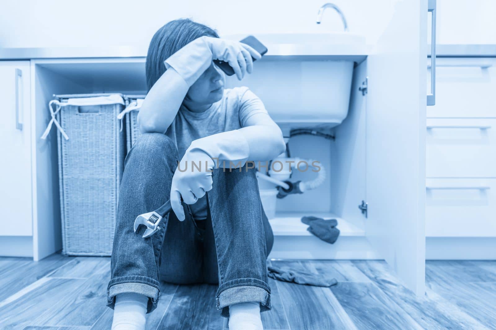 Woman sitting near leaking sink in laundry room holding adjustable wrench by Mariakray