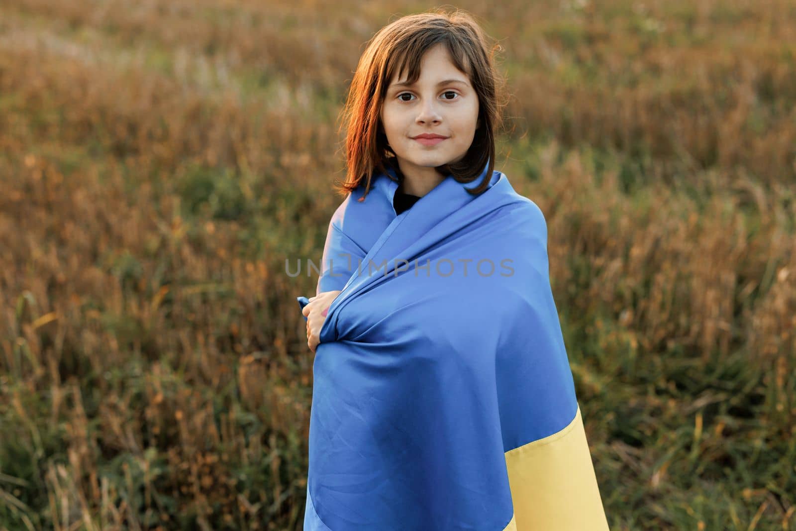 Portrait of Child with Ukrainian flag in field. Little girl waving national flag praying for peace. Happy kid celebrating Independence Day. Pray for Ukraine.