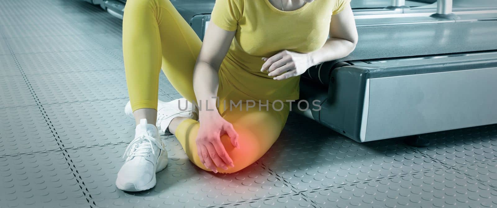 Young woman in sportswear having ache in knee while training in a gym, red spot showing pain