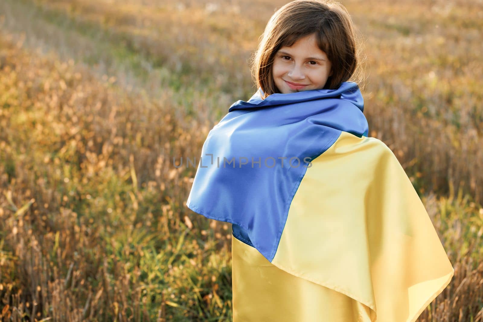 Portrait of teenager girl looking at camera wearing blue and yellow flag of Ukraine. Flag of Ukraine in hands of ukrainian girl. War in Ukraine. Support for Ukraine