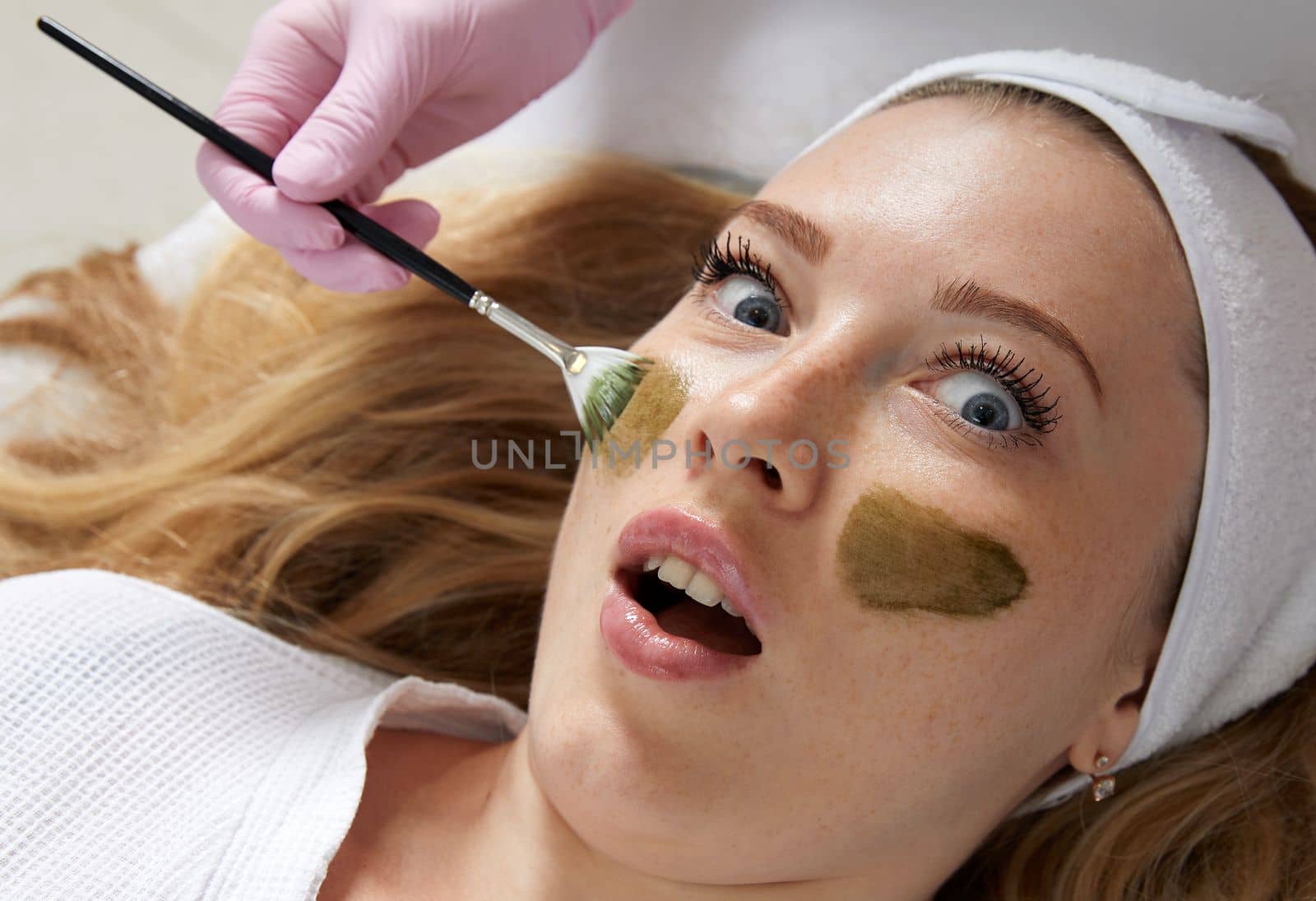 Cosmetologist applying a clay mask to the face of beautiful woman. Spa treatment in the beauty salon