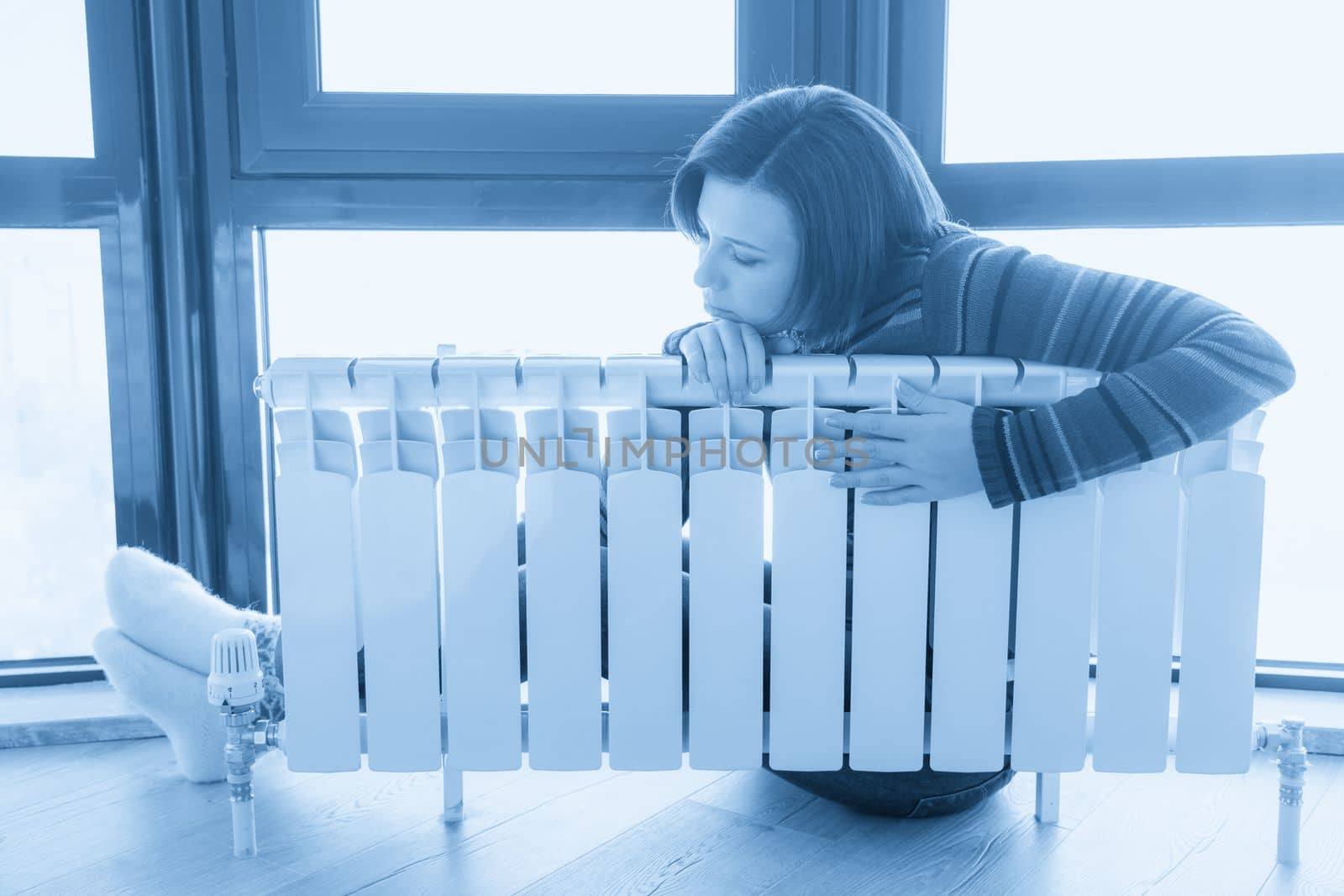 Woman wearing pullover sitting near heater radiator and hugs it by Mariakray