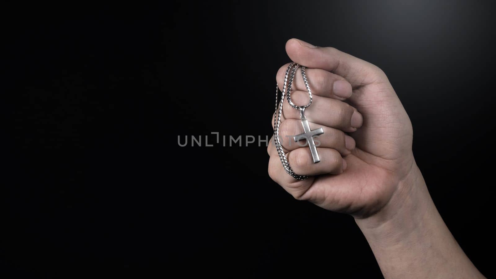 Close-up images of crucifix pendant and necklace in hand on black color background in studio which represent praying for god or jesus and thank gods for giving peaceful and faithful to people