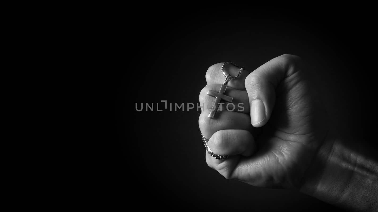 Close-up images of crucifix pendant and necklace in hand on black color background in studio which represent praying for god or jesus and thank gods for giving peaceful and faithful to people