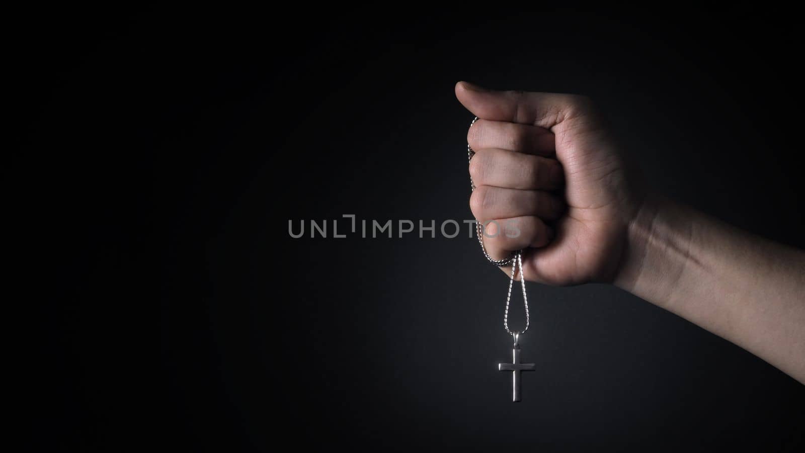 Close-up images of crucifix pendant and necklace in hand on black color background in studio which represent praying for god or jesus and thank gods for giving peaceful and faithful to people