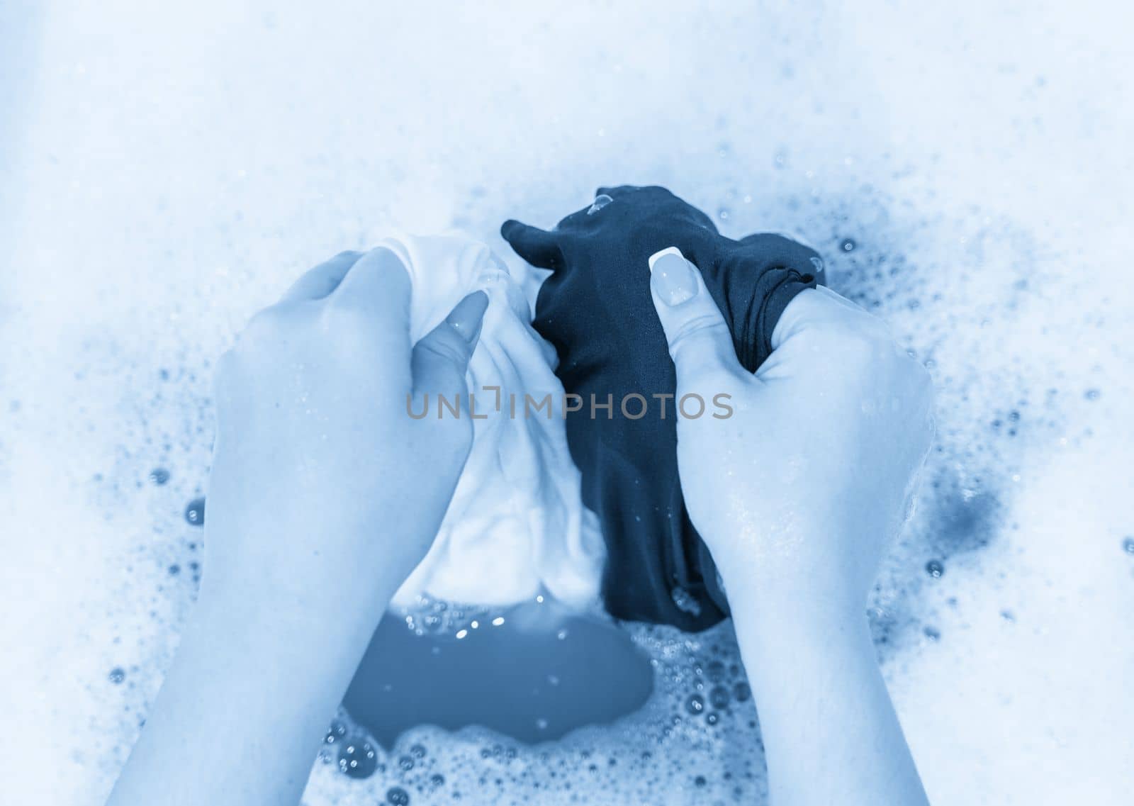 Hands holding black and white clothes while handwash in sink by Mariakray