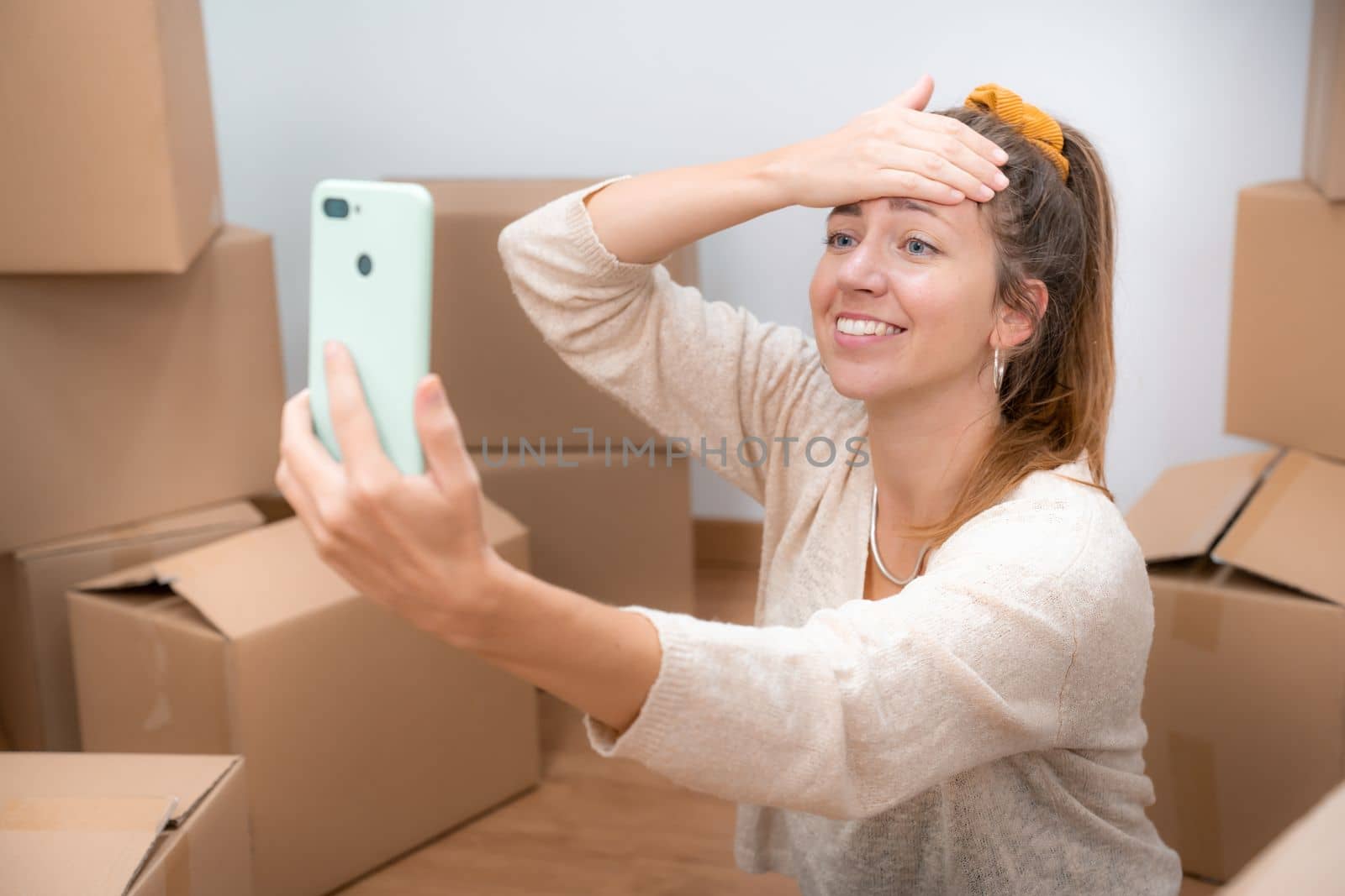 Beautiful girl with cardboard boxes unpacking in new home taking a selfie or video call with her family and friends. High quality photo
