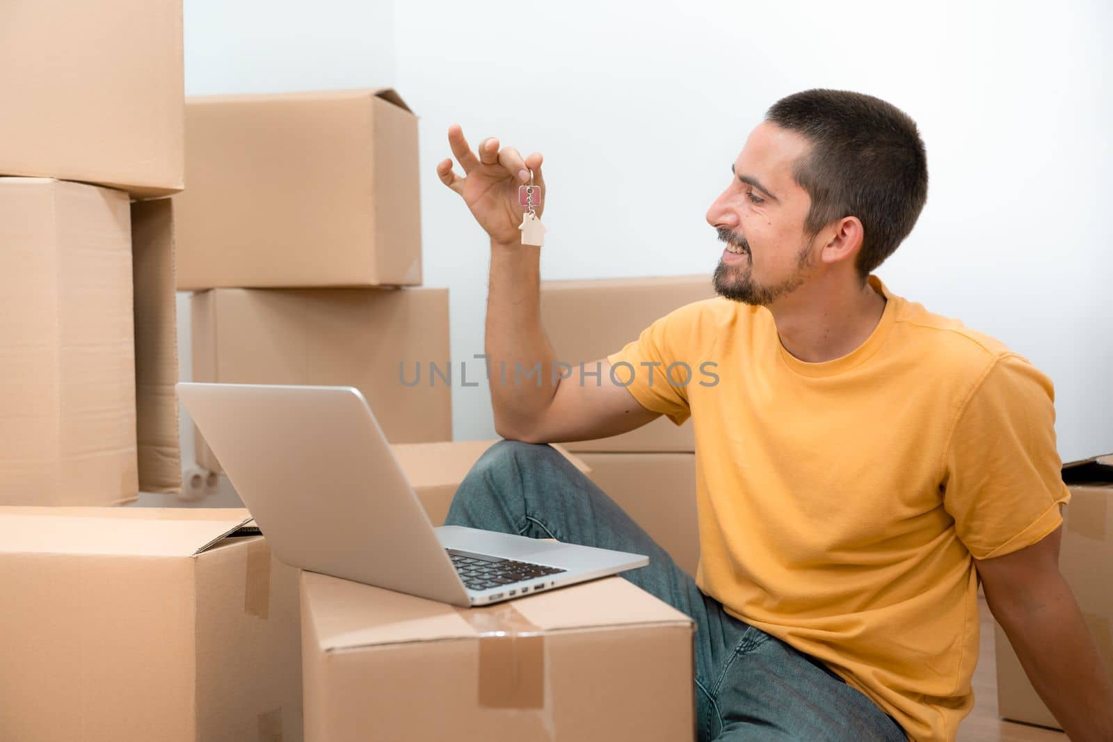 Happy caucasian man with the keys of his new home flat apartment house and laptop between boxes. High quality photo