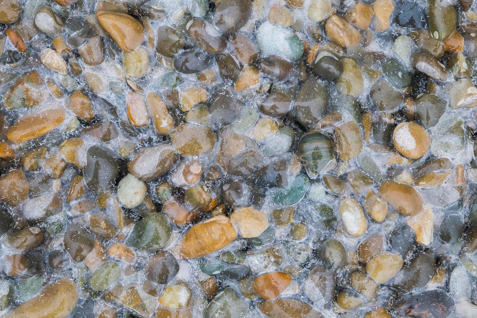 Frozen multicolored round cobblestones on the seashore.