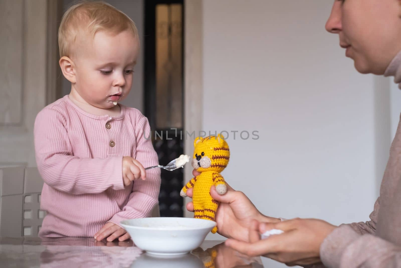 adorable little girl feeding tiger toy with spoon during breakfast