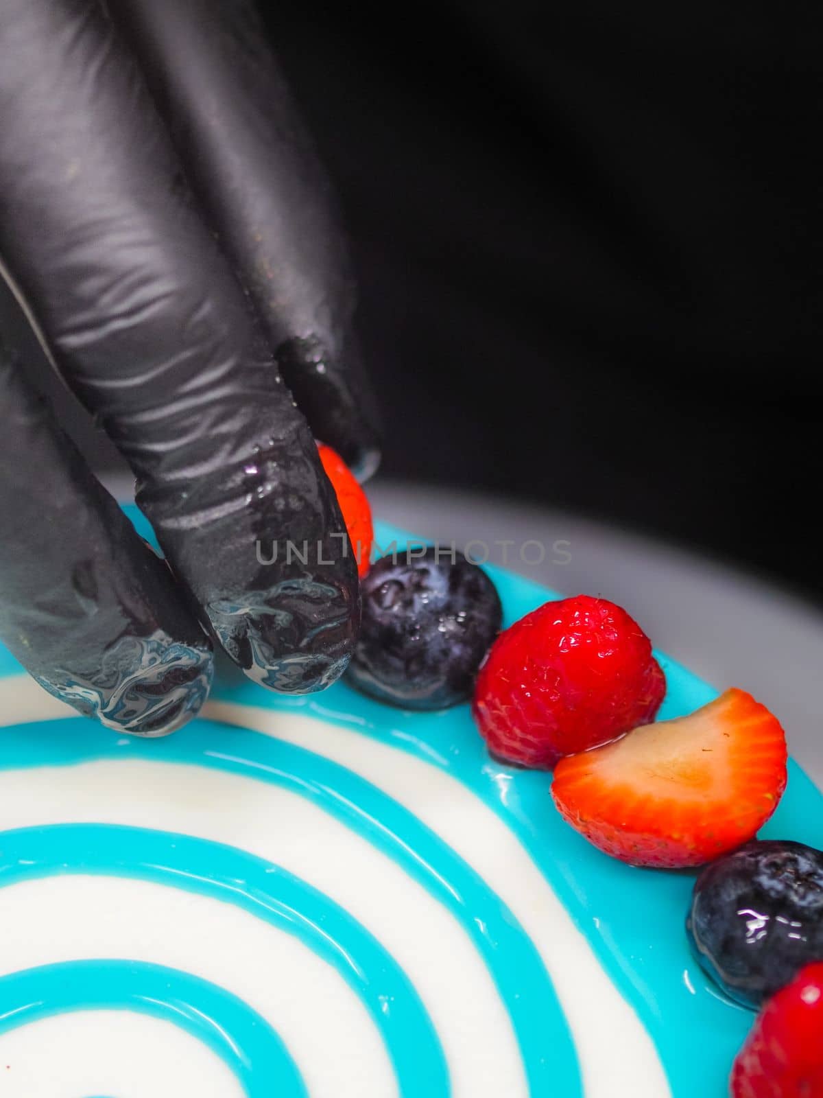 pastry chef cake designer decorating turquoise blue white frosted cheesecake in kitchen with piping bag