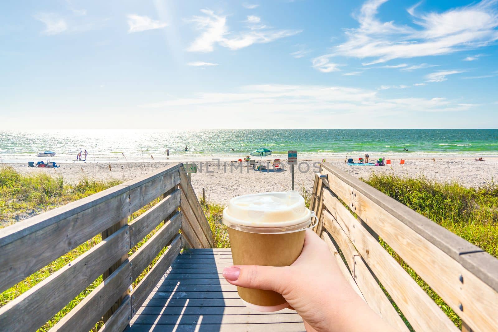 Indian rocks beach in Florida, USA with Hand holding paper cup of hot coffee by Mariakray