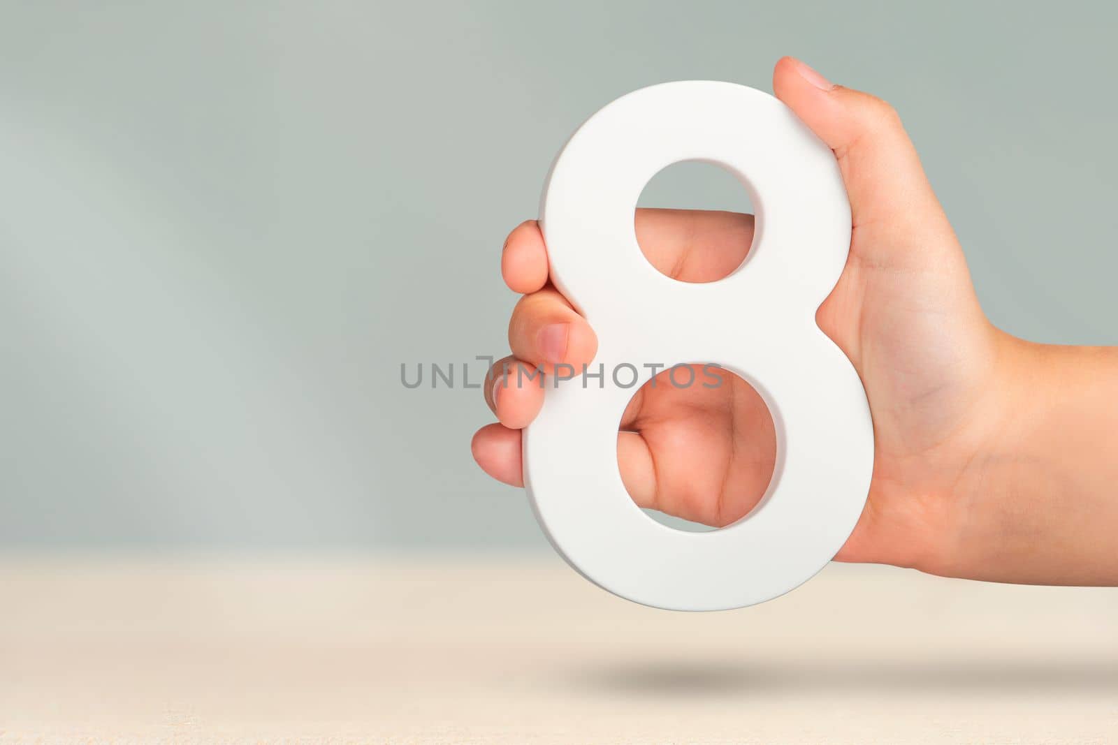 Eight in hand. A hand holds a white number 8 on a blurred background. Concept with number eight. Birthday 8 years, percentage, eighth grade or day, international women's day