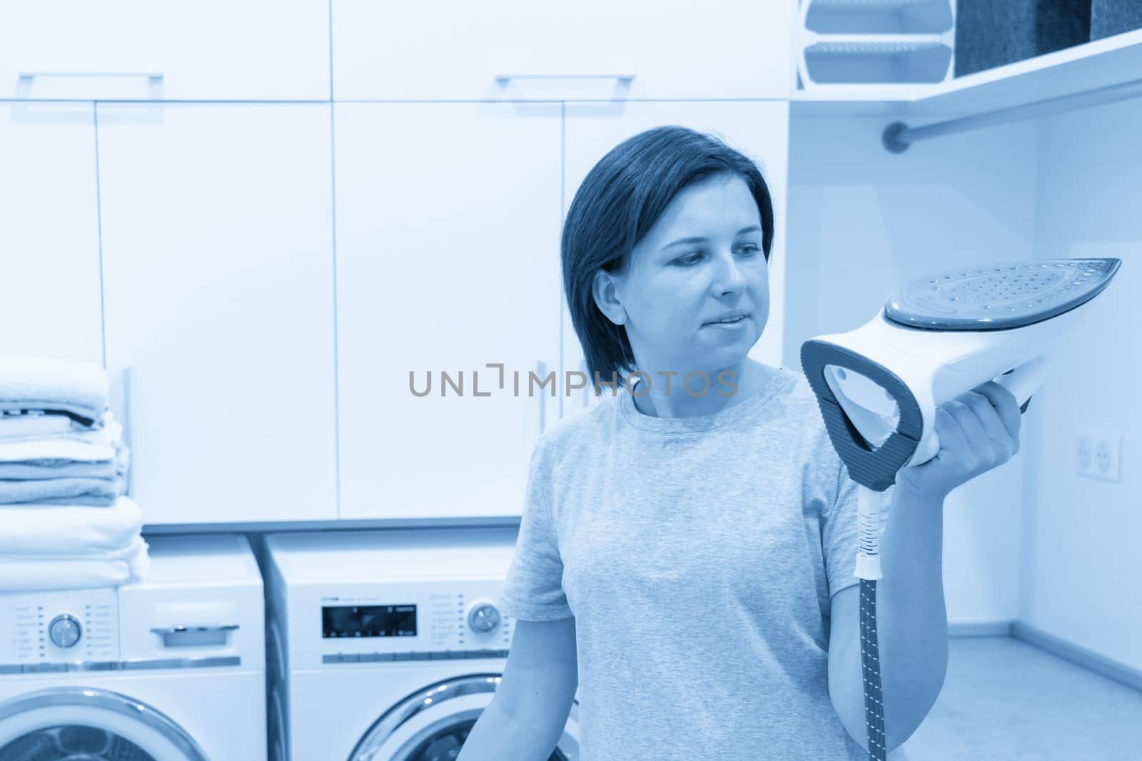Woman ironing white shirt on board in laundry room with washing machine