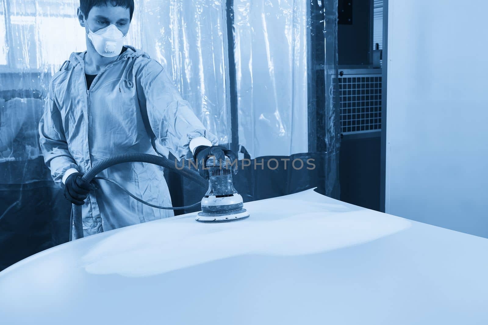 Auto mechanic wearing face mask buffing and polishing car hood in auto repair shop by Mariakray