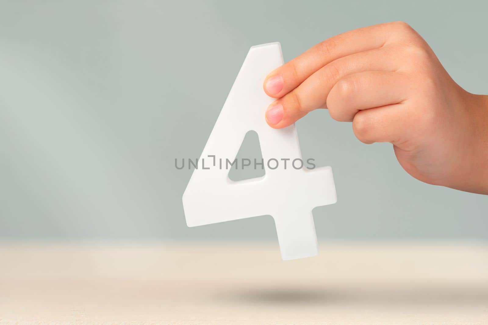 number four in hand. Hand holding white number 4 on blurred background with copy space. Concept with number four. Birthday 4 years, fourth grade, four day work week.