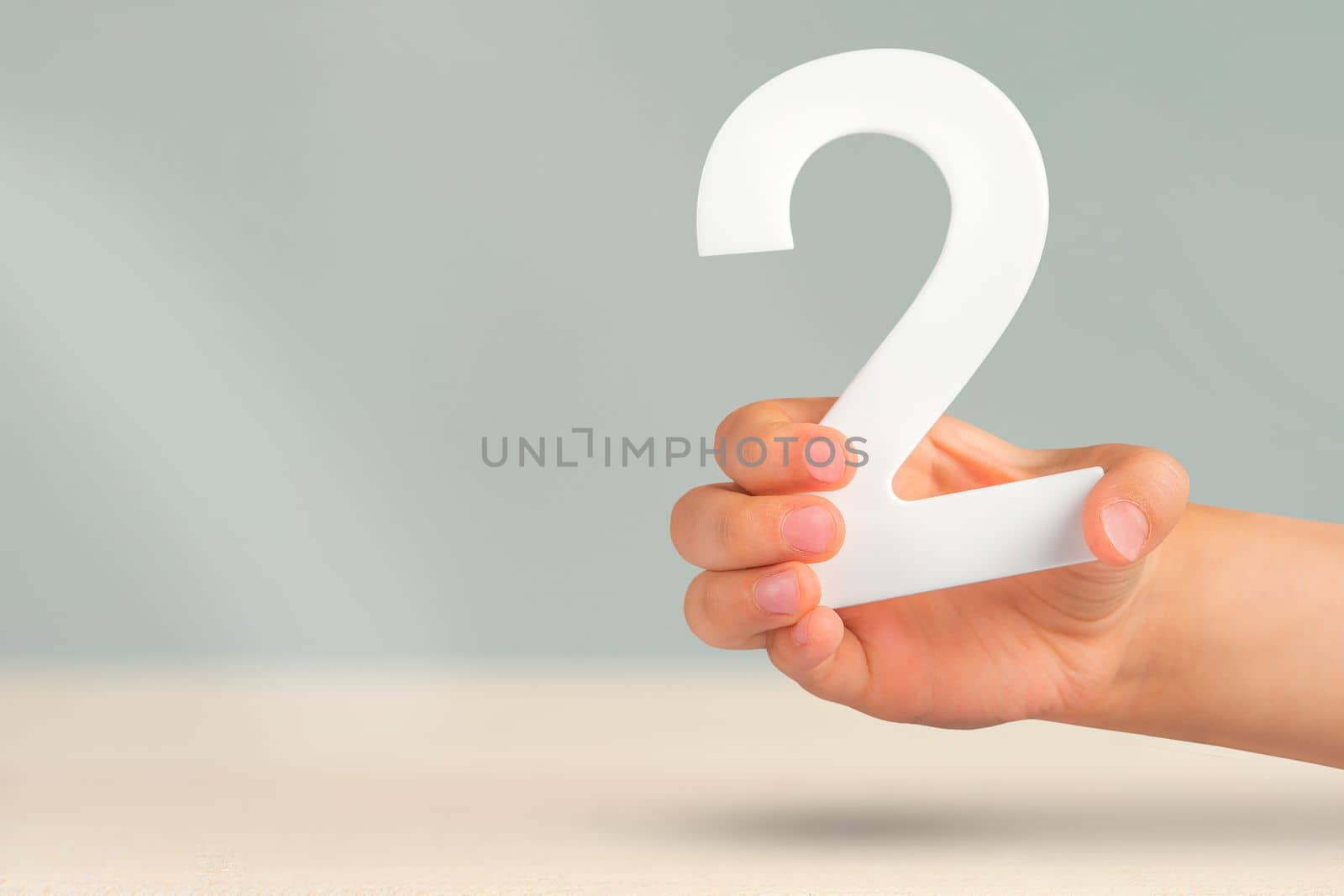 Number two in hand. Hand holding white number 2 on blurred background with copy space. Concept with number two. 2 percent, birthday 2 years old, couple, two, double.