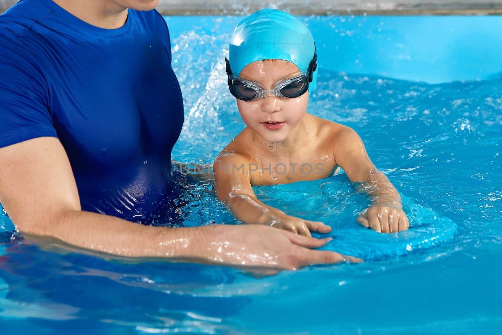 Male trainer teaching boy how to swim in indoor pool with pool flutter board