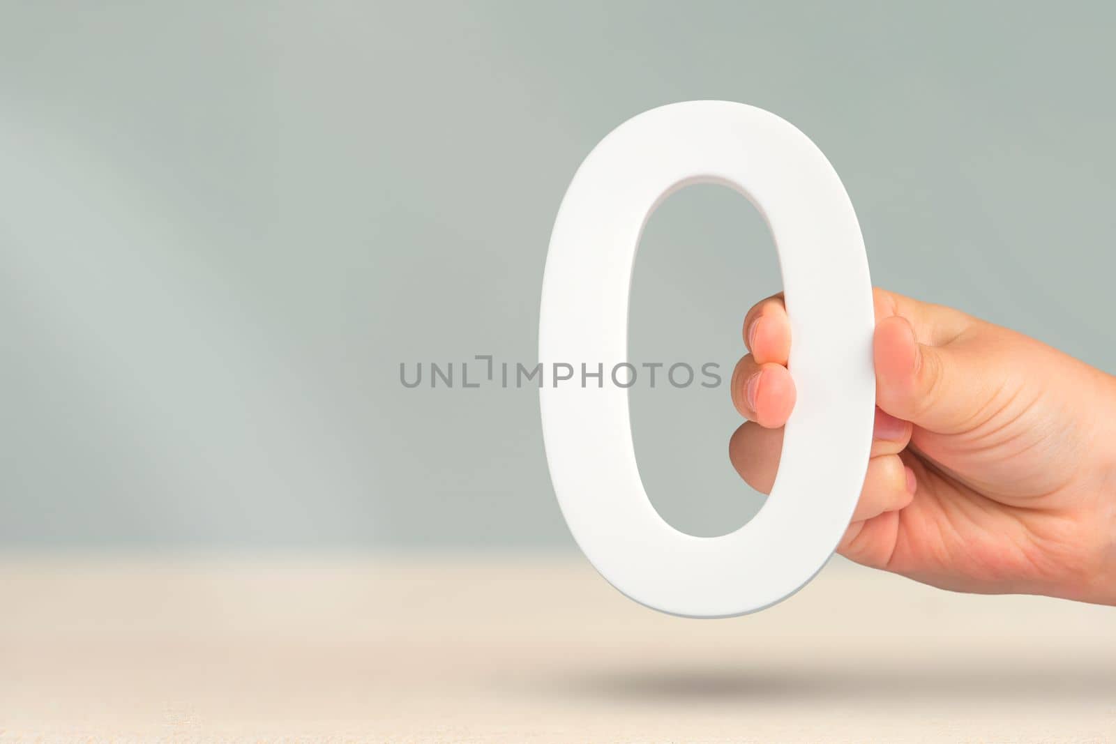 Numeral zero in hand. A hand holds a white number zero on a blurred background with copy space. Zero concept, 0 percent interest rate, minimum air emissions, cost or credit no increase