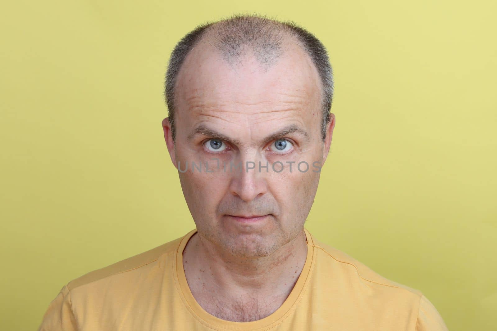 Attractive man in yellow T-shirt on yellow background looking into camera.