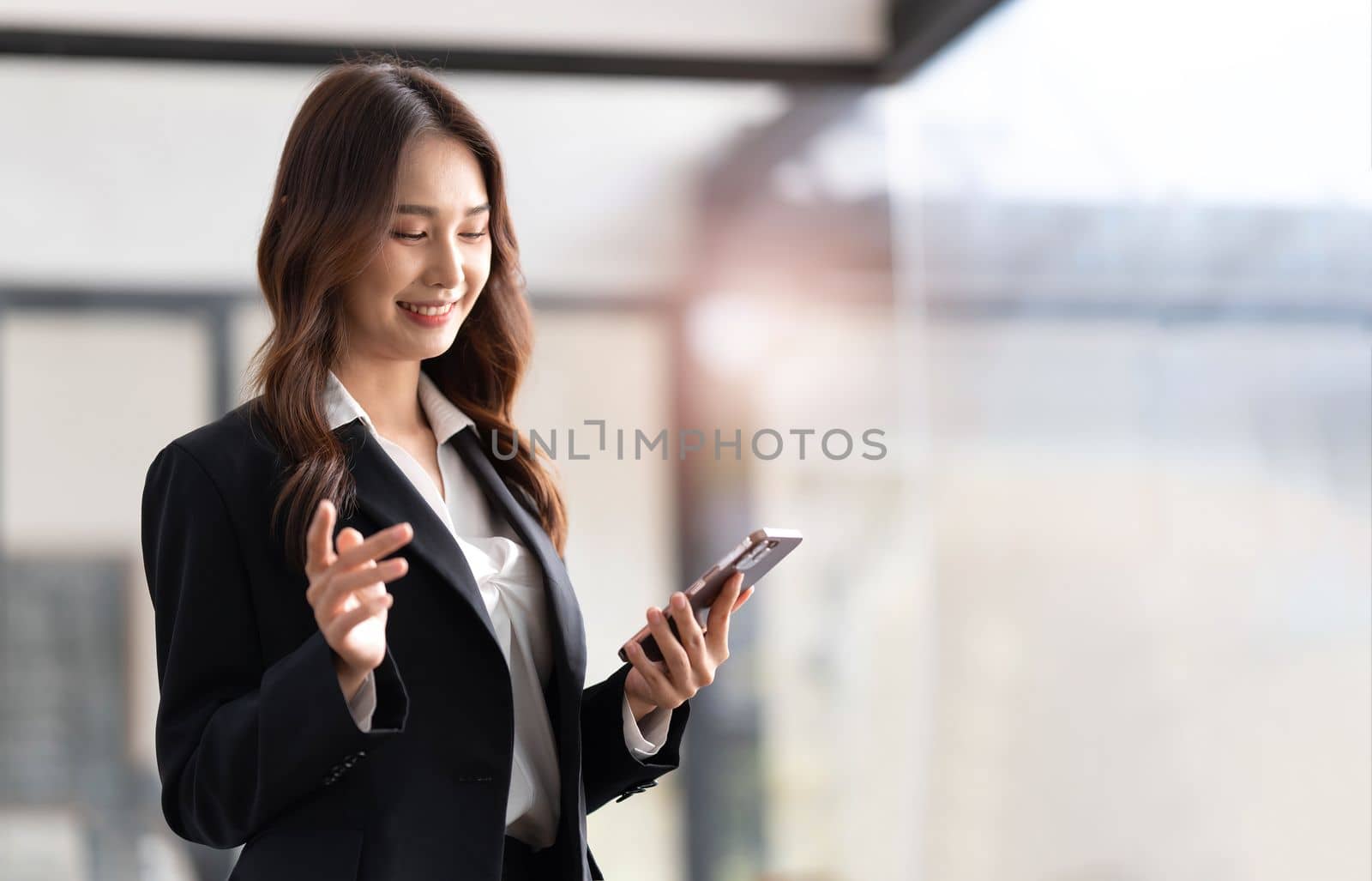 Image of a young Asian businesswoman standing using mobile phone at the office...