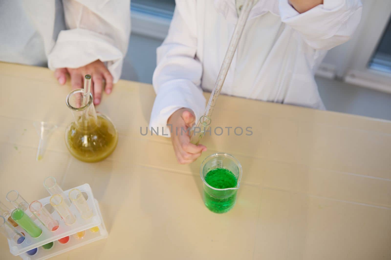 Selective focus: kids performing chemical experiments, using graduated pipette, beaker, test tubes at chemistry class by artgf