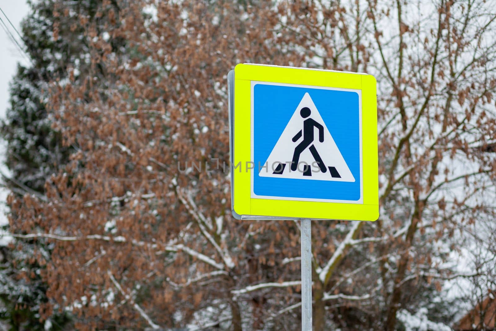 A road sign of a pedestrian crossing in close-up. A sign with a reflective coating is installed on the street and intersection and warns drivers about a pedestrian crossing. Be careful on the road
