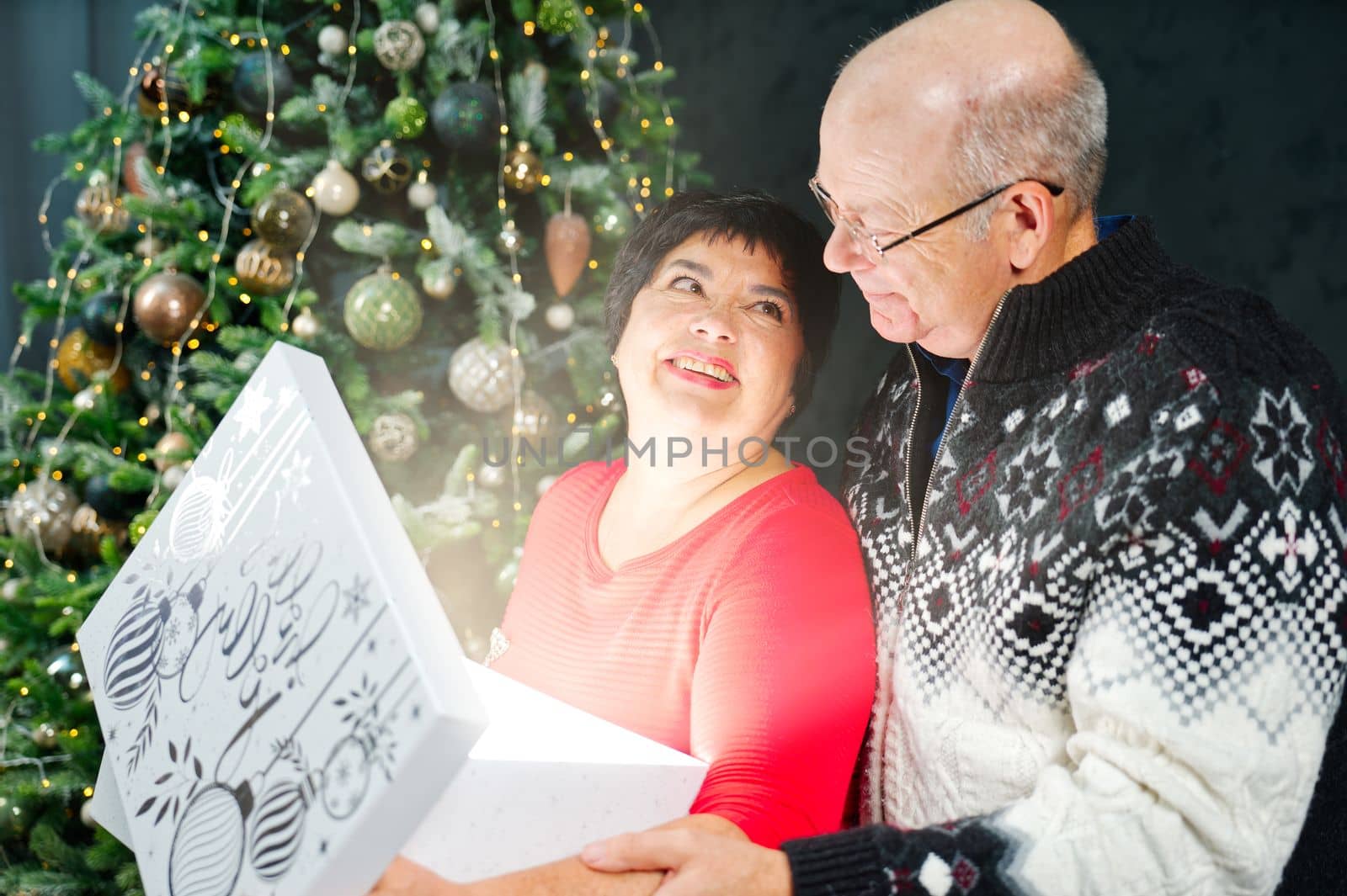 Man 60s giving a Christmas present to his woman. Great xmas surprise Beautiful woman 60s opening a gift box and smiling while her boyfriend hug her. Christmas wonder concept