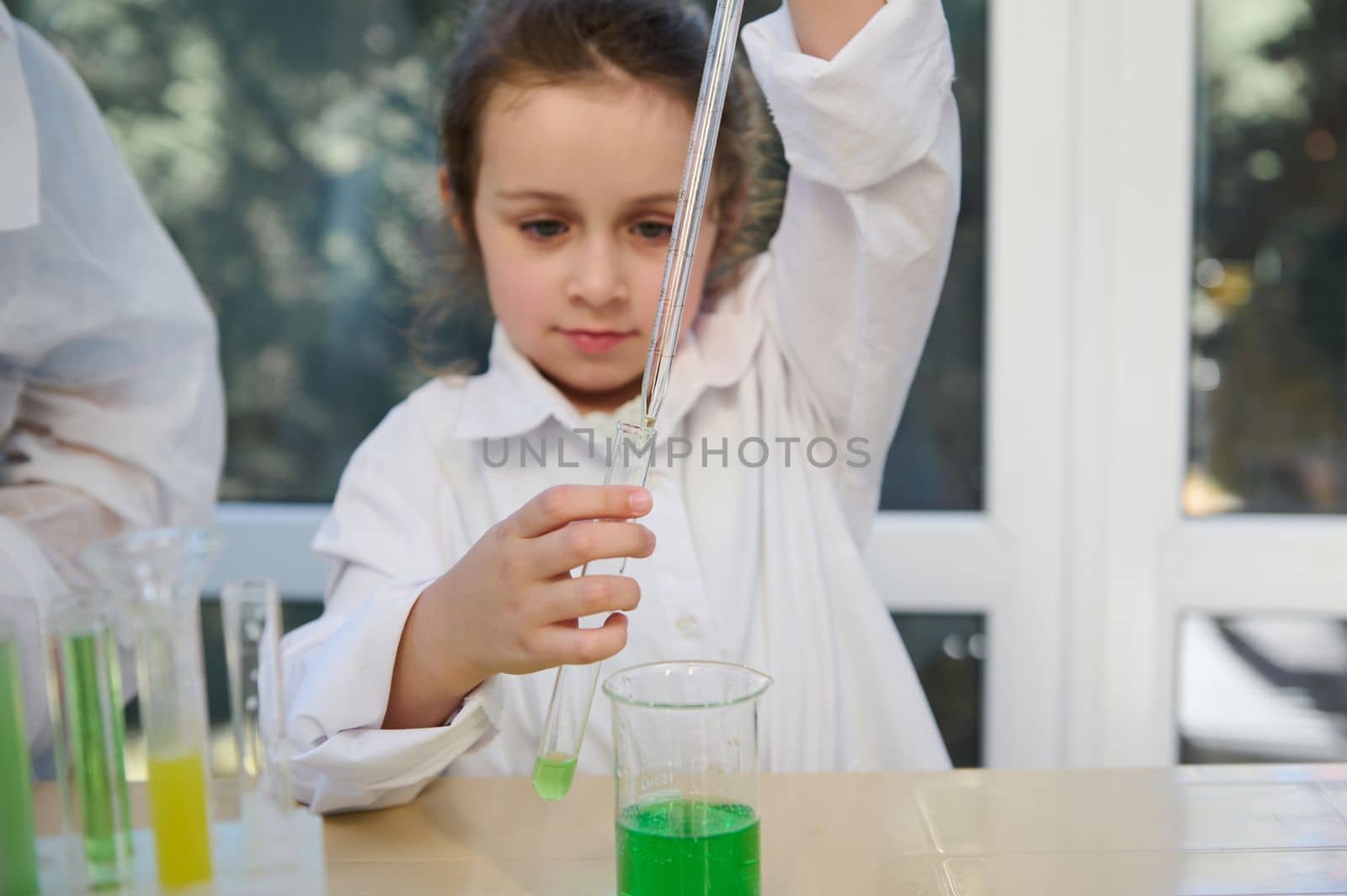 Selective focus on the hands of a smart schoolkid using graduated pipette, dripping few reagents into a test tube with chemical fluid substances. Children learning chemistry in school laboratory