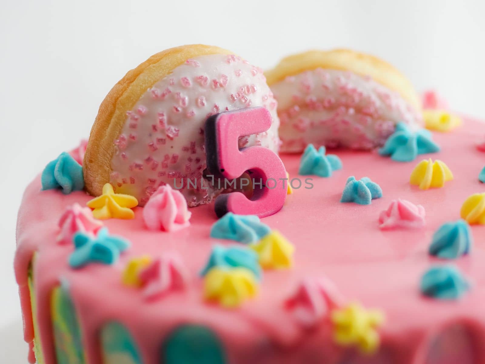 Close up of pink frosted dripping cake with donut and plastel brushed royal star sprinkles insolated on white studio shot