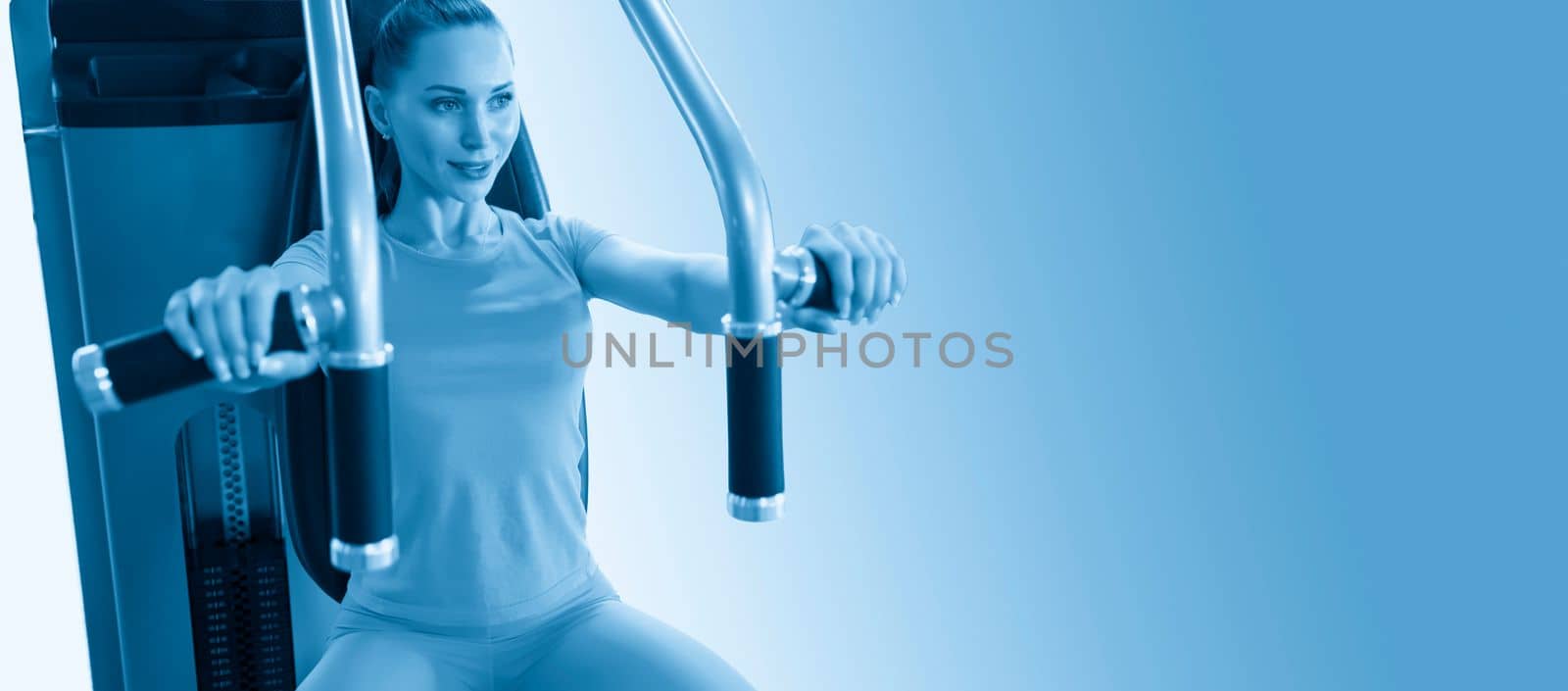 Portrait of Cheerful young adult caucasian woman working out on exercise machine cut out on blue background by Mariakray