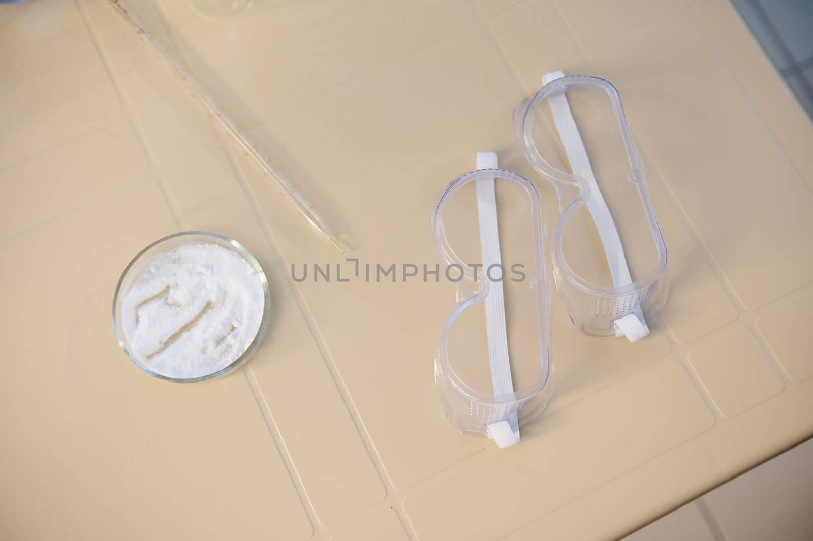 Top view - protective goggles near Petri dish with white powder, on a plastic table in the chemistry laboratory by artgf