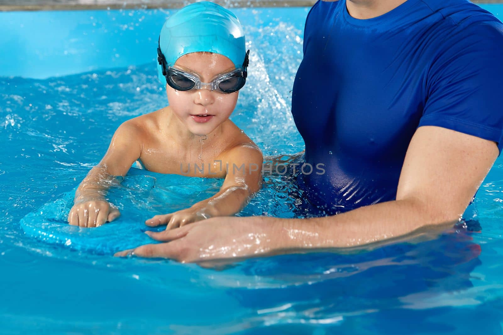 Little boy learning to swim in indoor pool with pool board. Swimming lesson. Active child swims in water