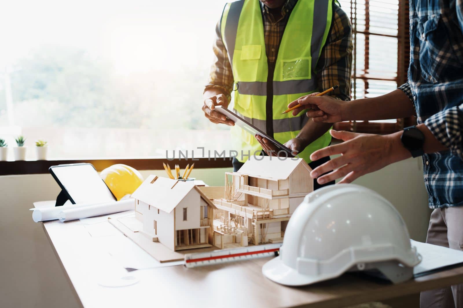 Engineers are consulting the team to design an architectural structure for clients with blueprints and building models to work at office.