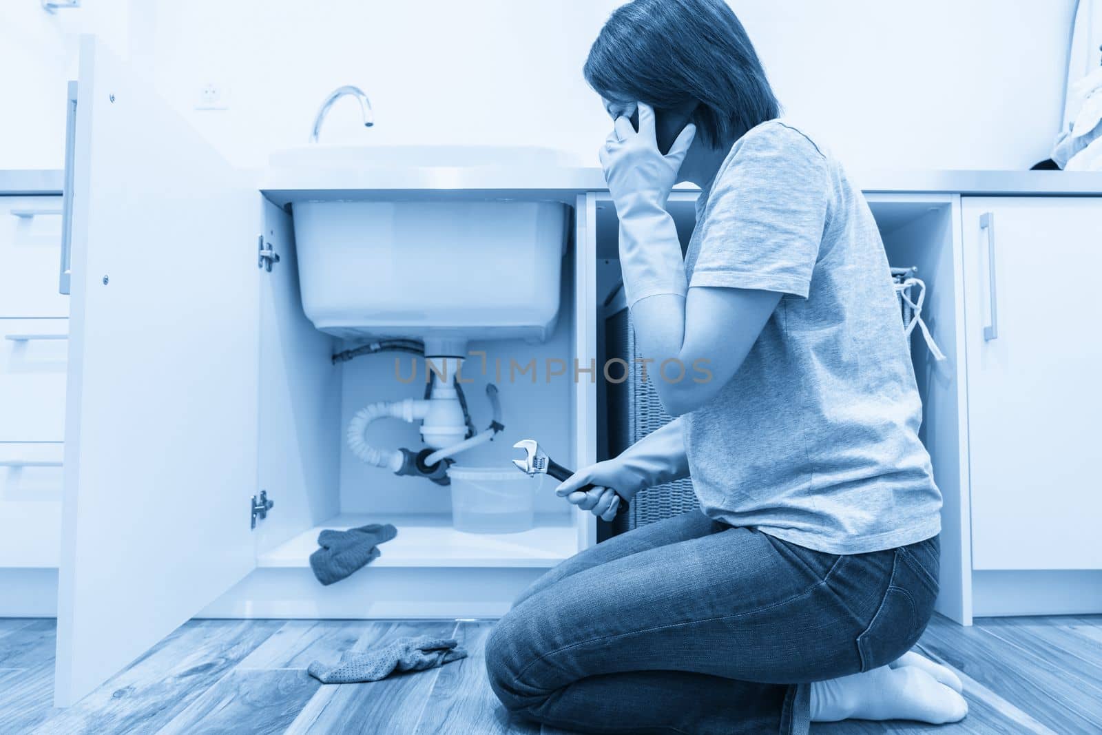 Woman sitting near leaking sink calling for help
