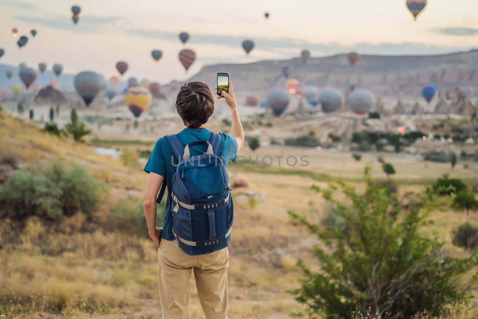 Tourist man looking at hot air balloons in Cappadocia, Turkey. Happy Travel in Turkey concept. Man on a mountain top enjoying wonderful view.