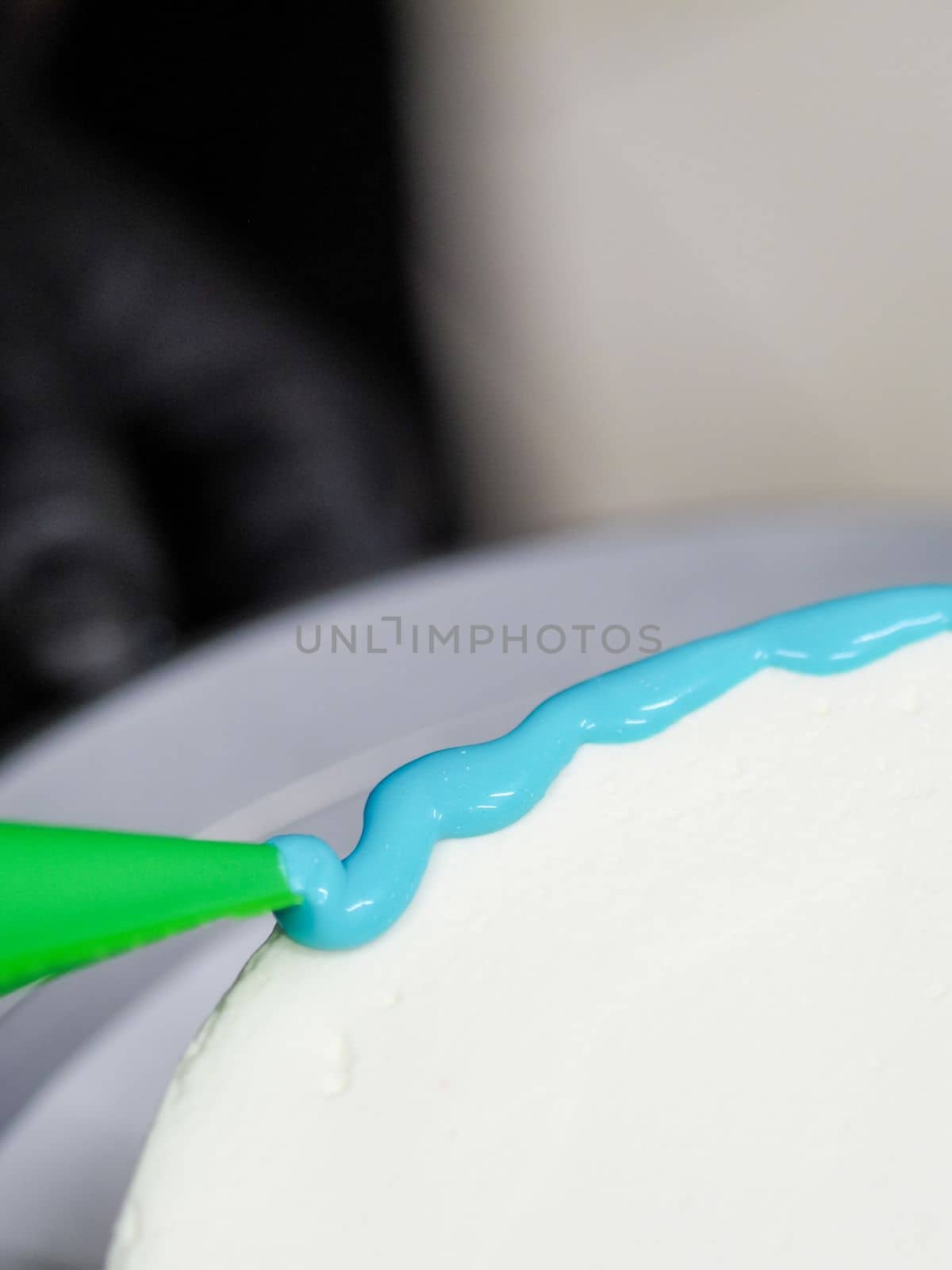 hand pastry chef designer topping a frosted white cake with pastel light blue drip filling bag by verbano