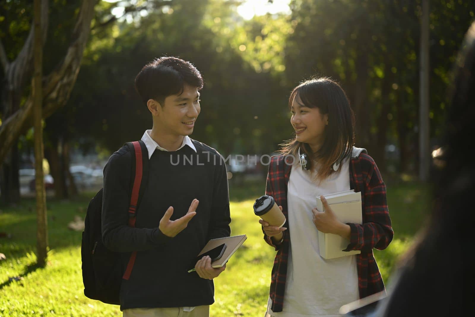 Smiling asian woman university student walking in campus and talking to her friend about exam results by prathanchorruangsak