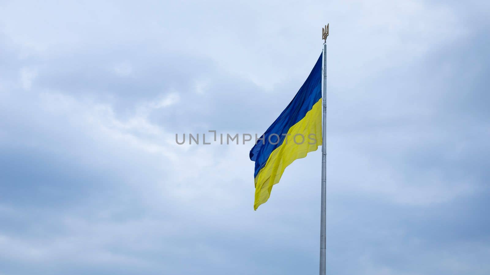 The Ukrainian flag of blue and yellow national colors on the flagpole flutters in the wind against the blue sky and the morning rising sun. The official state symbol of Ukrainians. Patriotism