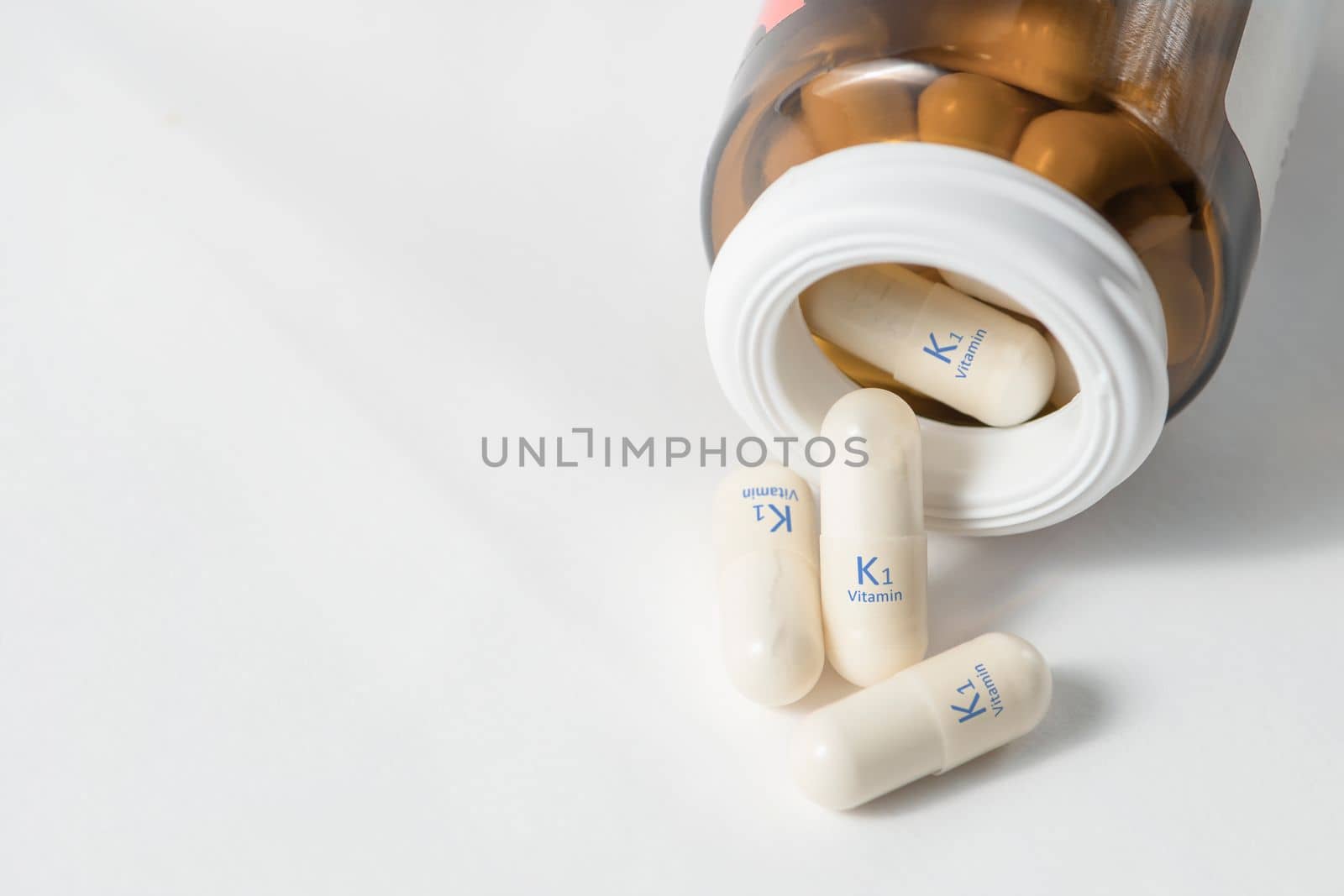 Vitamin K1.Capsules with phylloquinone increase blood clotting, stimulate wound healing. White capsules of vitamin K1 or phylloquinone are scattered on the table with copy space on a white background