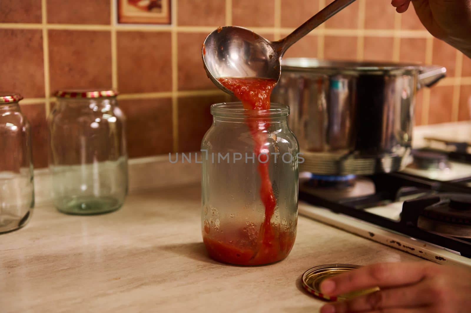 Close-up cooking, canning homemade passata from organic ripe juicy tomatoes for the winter. Canning food. Making preserves. Conservation. Housewife pouring boiling tomato juice into a sterilized jar