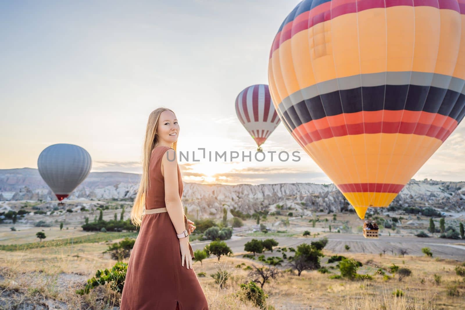 Tourist woman looking at hot air balloons in Cappadocia, Turkey. Happy Travel in Turkey concept. Woman on a mountain top enjoying wonderful view.